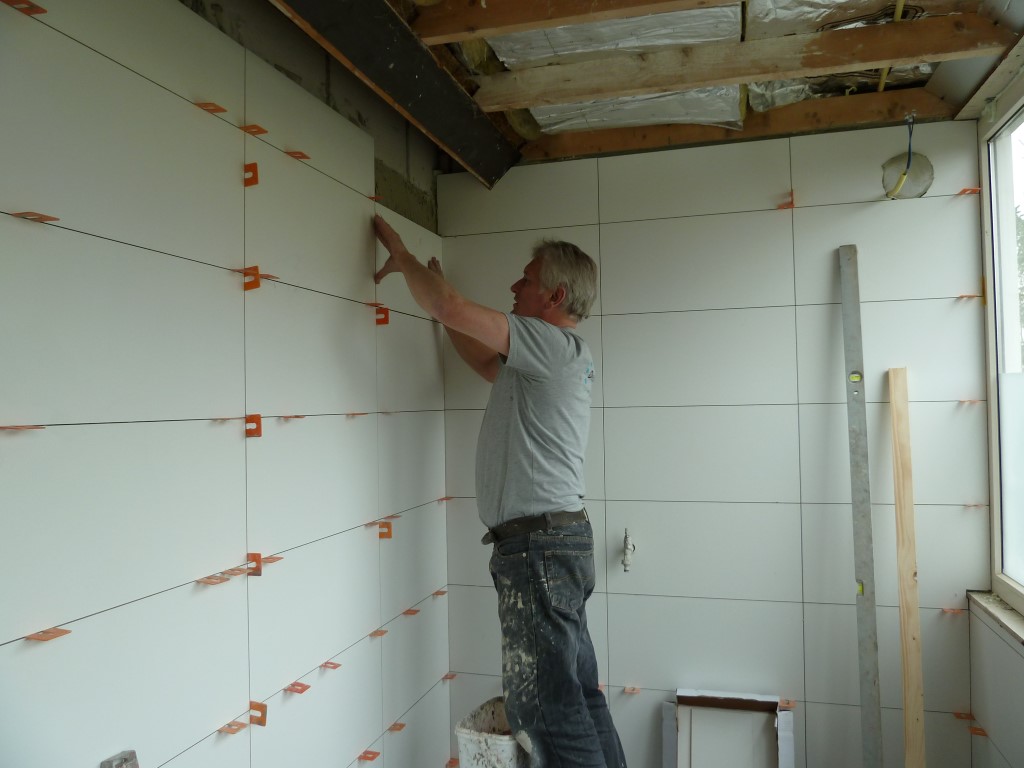 Gerard zet tegels op de wand van een badkamer in aanbouw